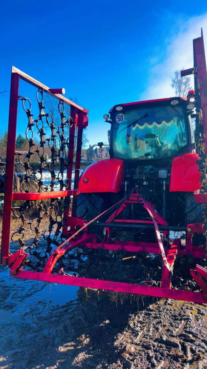 Tracteur agricole rouge équipé d’une herse métallique Puy-de-Dôme